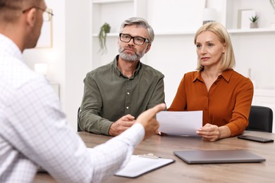 Photo of Pension plan. Couple consulting with insurance agent at table indoors