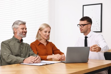 Pension plan. Couple consulting with insurance agent at table indoors