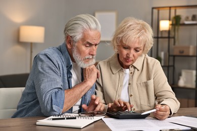 Photo of Pension savings. Senior couple planning budget at wooden table indoors