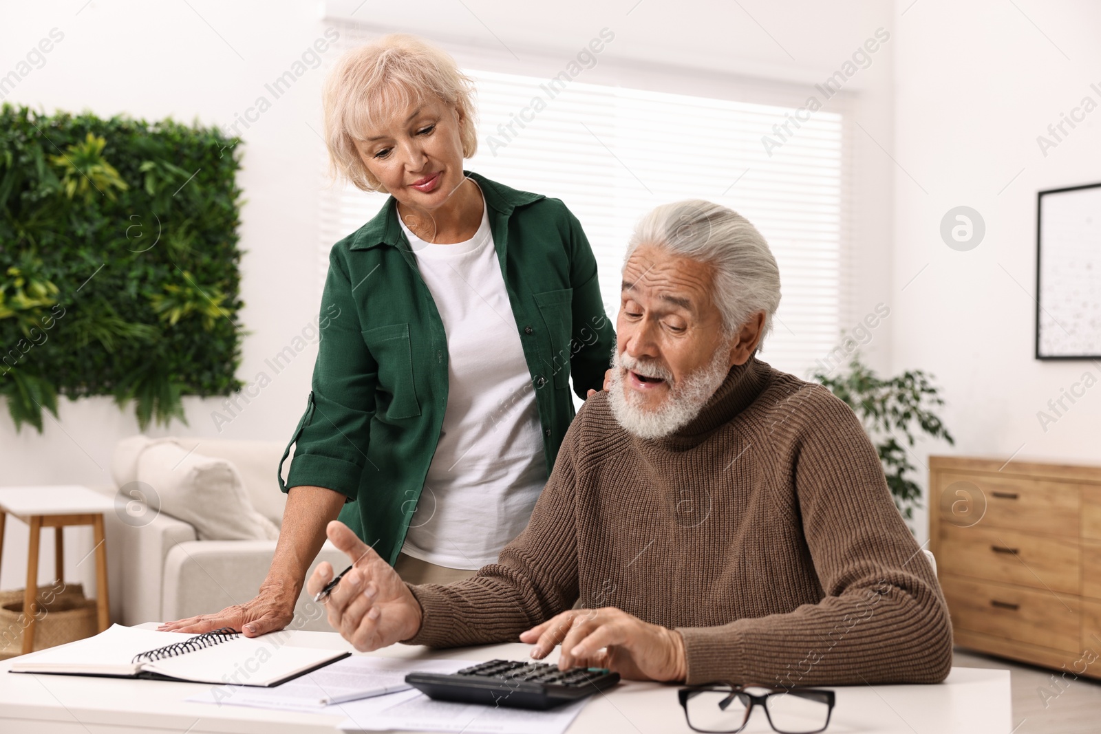 Photo of Pension savings. Senior couple planning budget at white table indoors