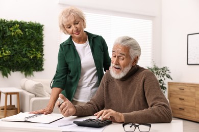 Photo of Pension savings. Senior couple planning budget at white table indoors