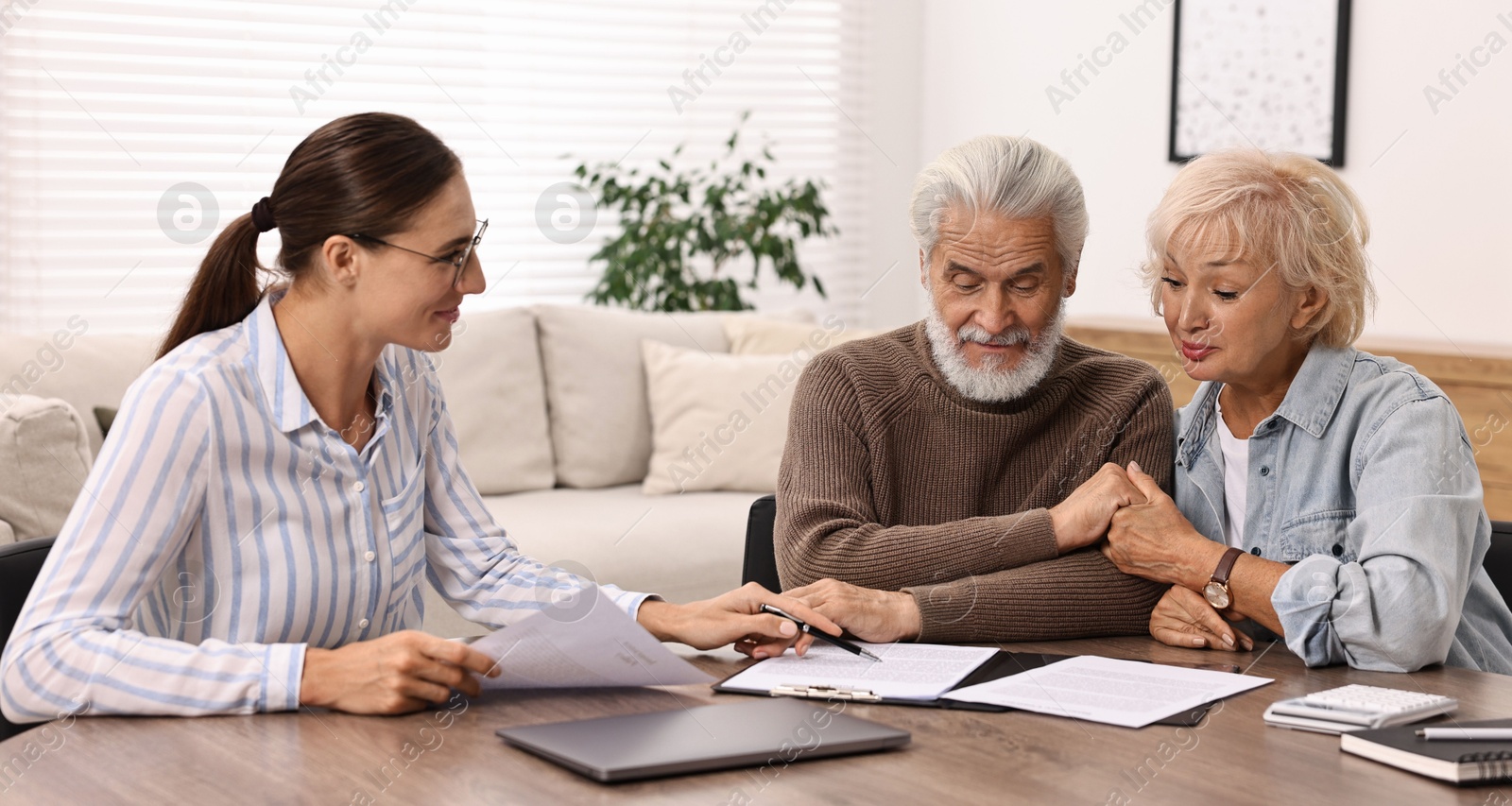 Photo of Pension plan. Senior couple consulting with insurance agent at wooden table indoors