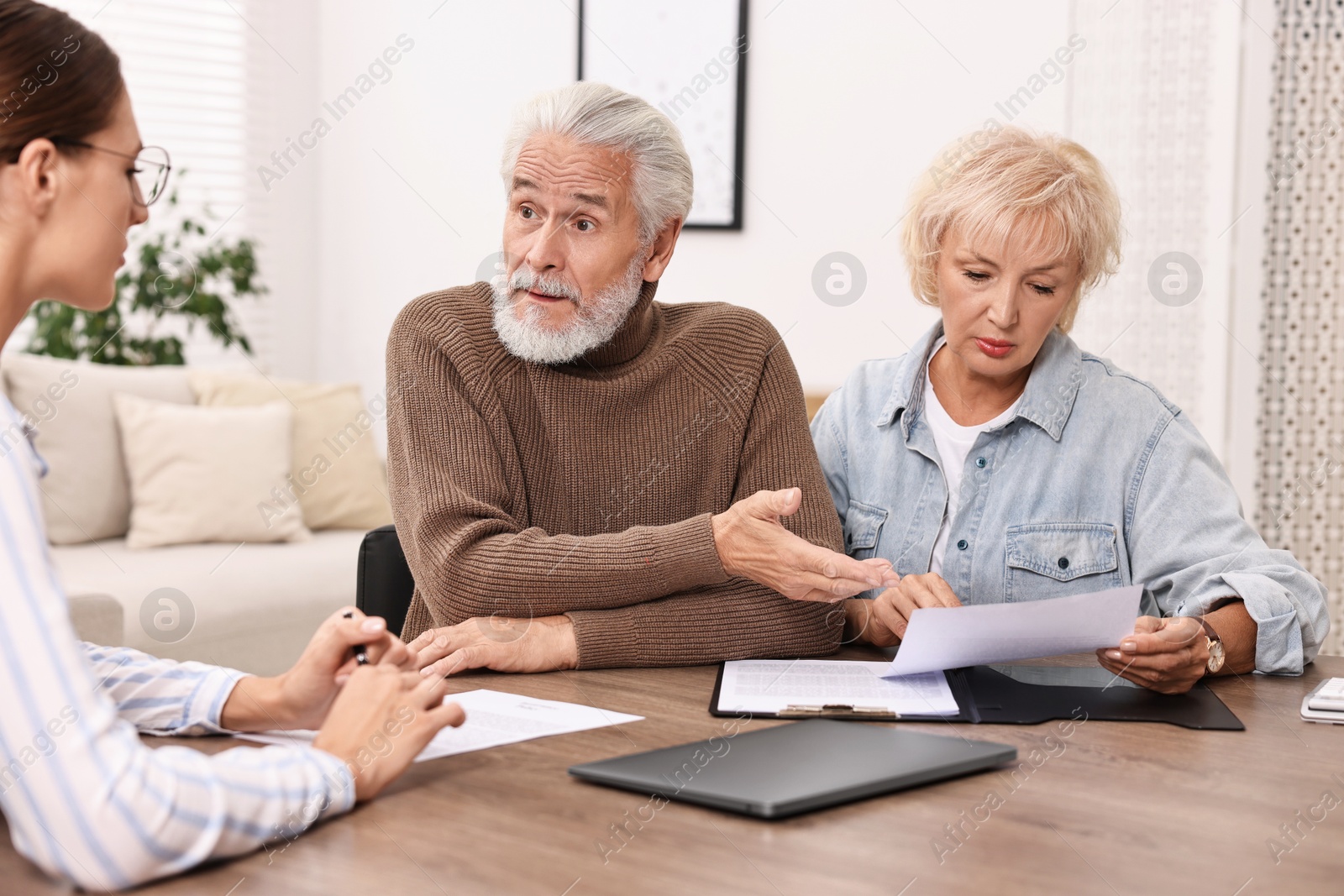 Photo of Pension plan. Senior couple consulting with insurance agent at wooden table indoors