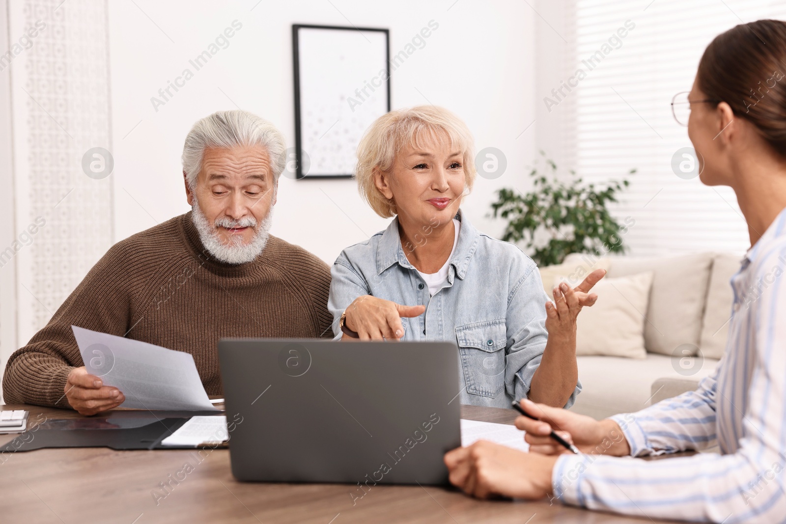 Photo of Pension plan. Senior couple consulting with insurance agent at wooden table indoors