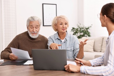 Pension plan. Senior couple consulting with insurance agent at wooden table indoors