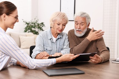 Pension plan. Senior couple consulting with insurance agent at wooden table indoors