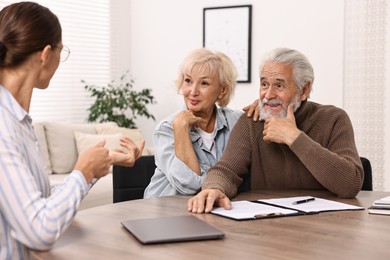 Pension plan. Senior couple consulting with insurance agent at wooden table indoors