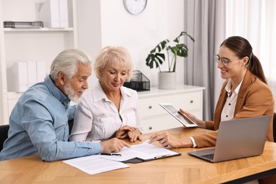 Pension plan. Senior couple consulting with insurance agent at wooden table indoors