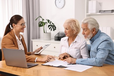 Pension plan. Senior couple consulting with insurance agent at wooden table indoors