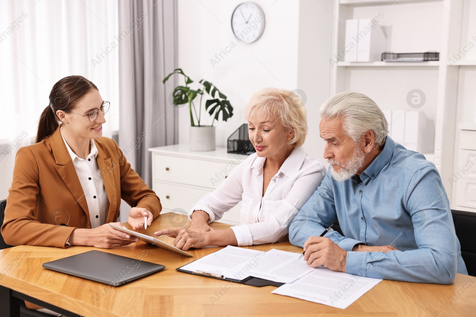 Photo of Pension plan. Senior couple consulting with insurance agent at wooden table indoors