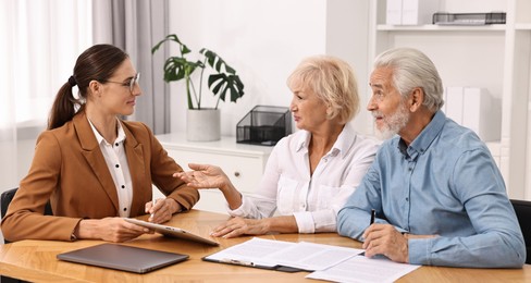 Pension plan. Senior couple consulting with insurance agent at wooden table indoors