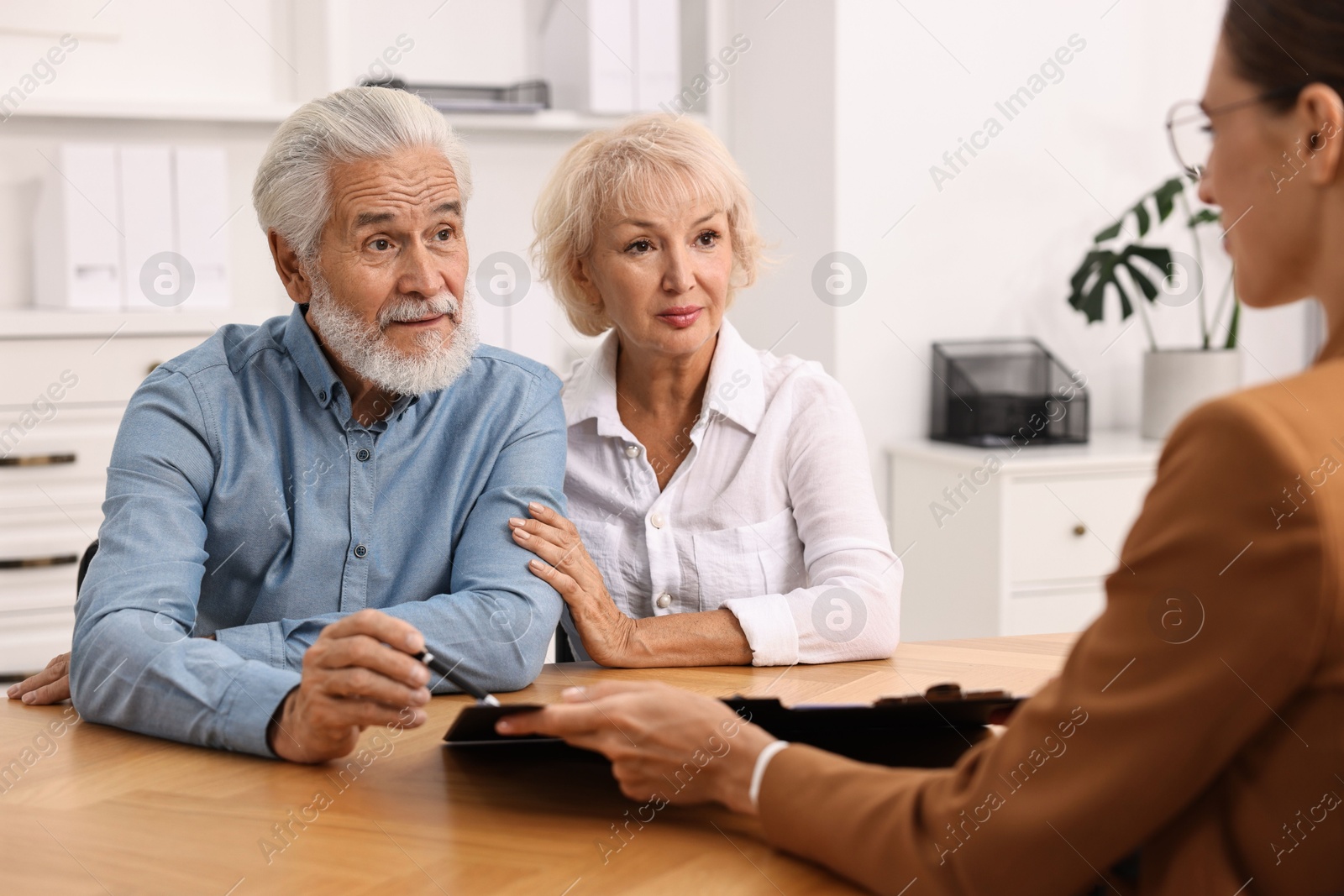 Photo of Pension plan. Senior couple consulting with insurance agent at wooden table indoors