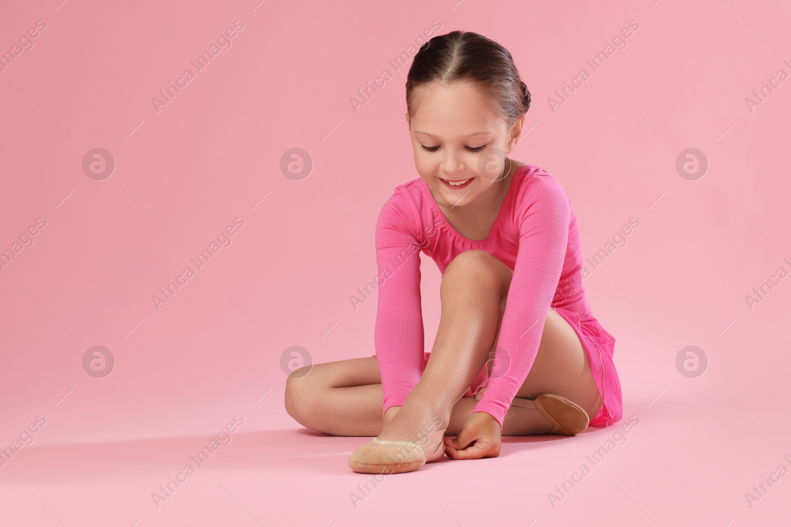 Photo of Little ballerina putting on pointe shoes against pink background, space for text