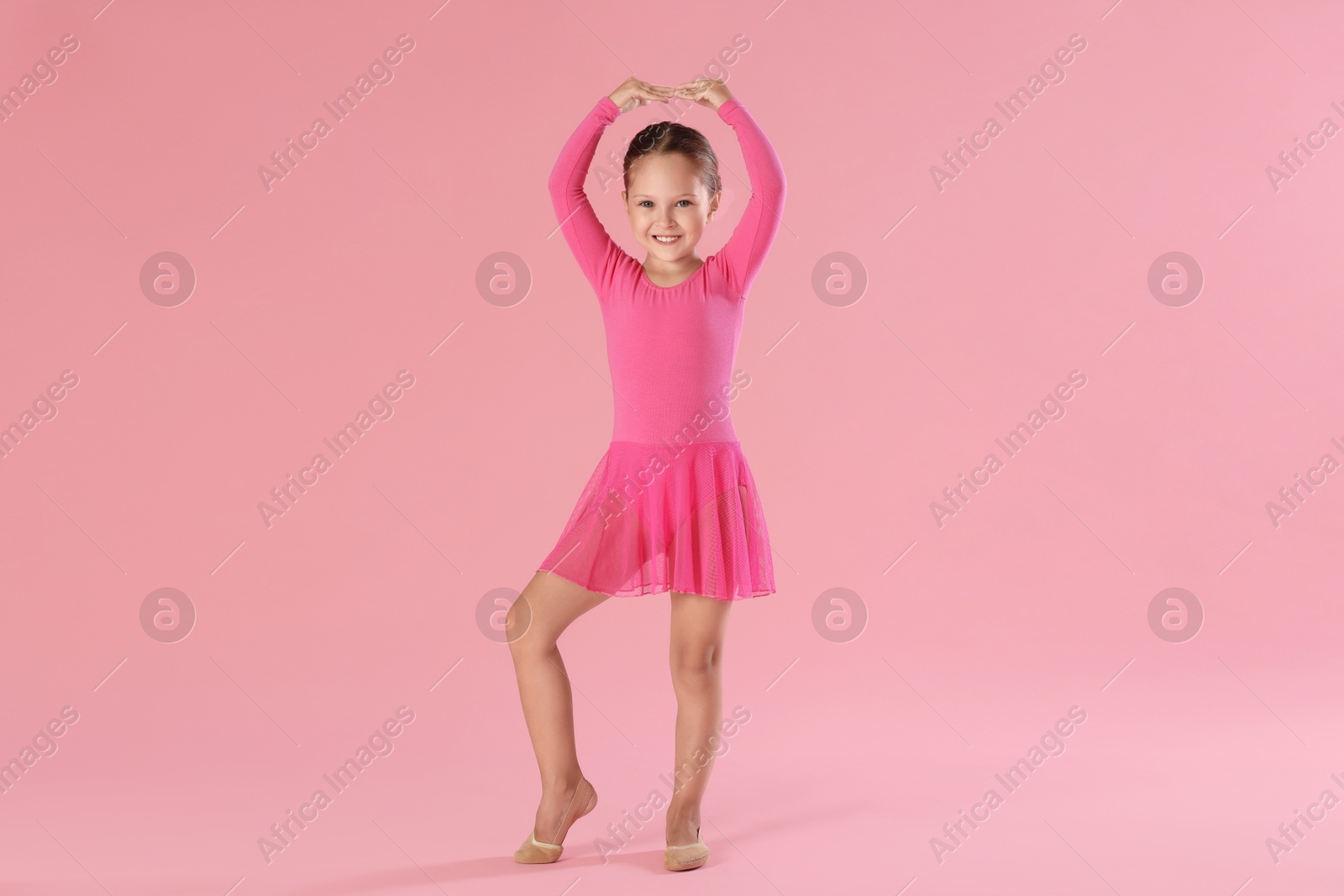 Photo of Little ballerina practicing dance moves on pink background