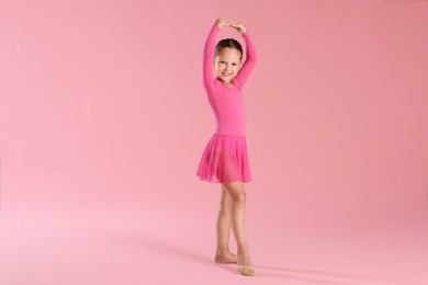 Little ballerina practicing dance moves on pink background