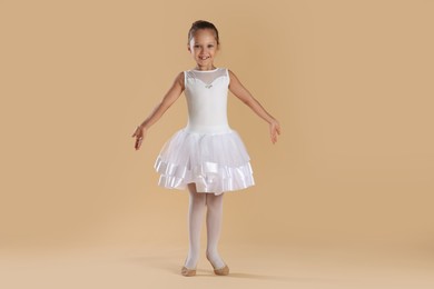 Little ballerina practicing dance moves on beige background