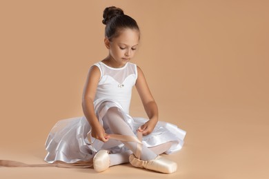 Photo of Little ballerina tying pointe shoes on beige background