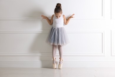 Photo of Little ballerina practicing dance moves near white wall indoors