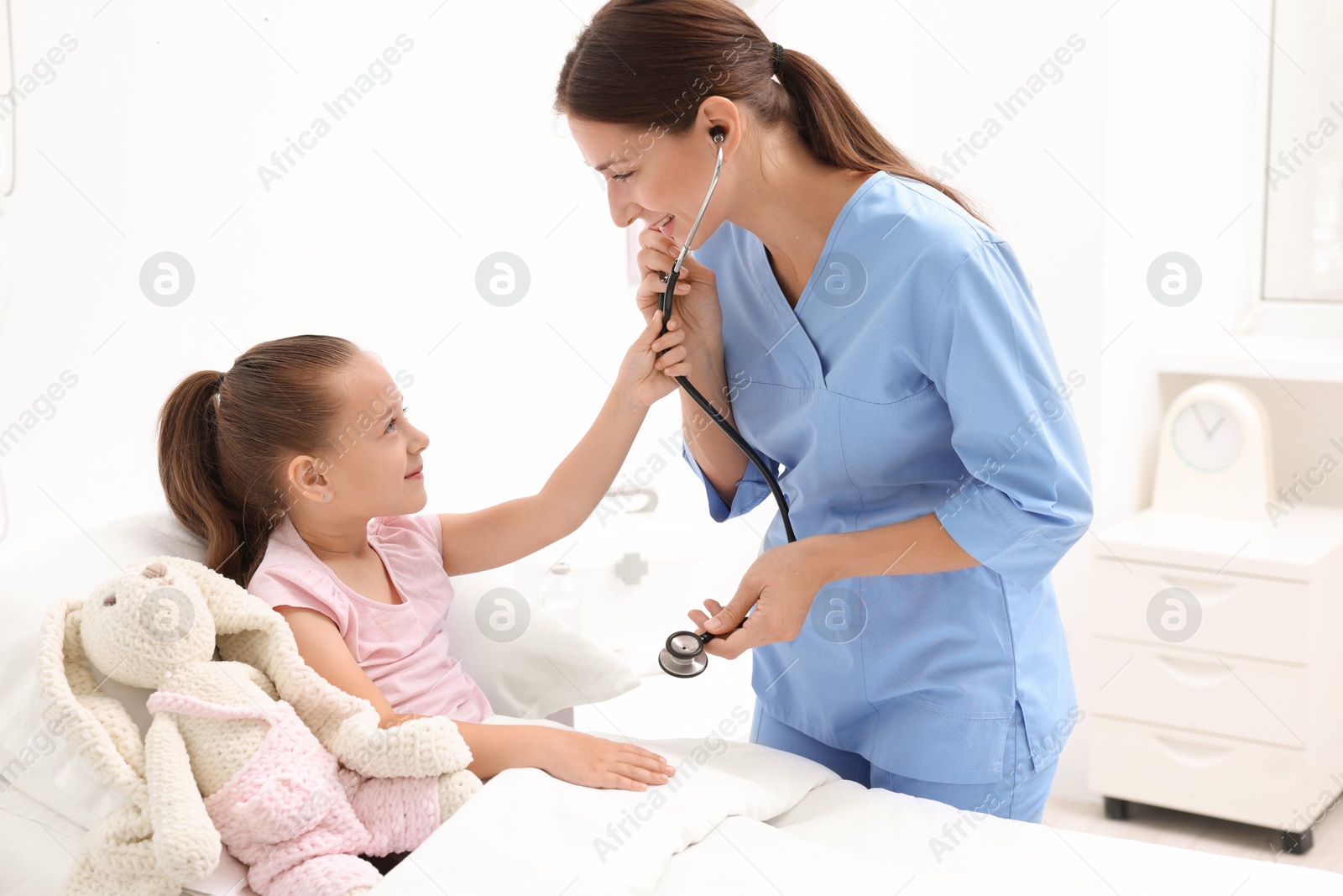 Photo of Doctor examining little girl on bed at hospital