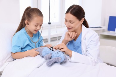 Photo of Doctor examining little girl on bed at hospital