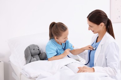 Doctor examining little girl on bed at hospital