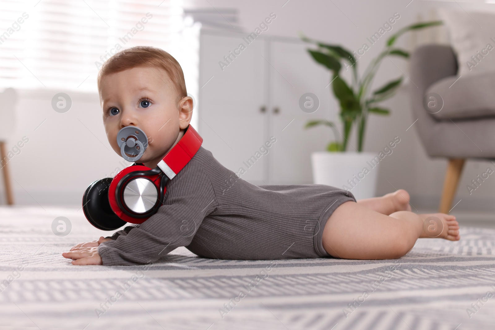 Photo of Cute little baby with pacifier and headphones on floor at home