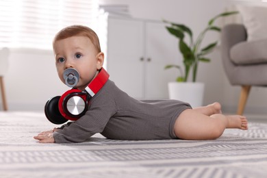 Cute little baby with pacifier and headphones on floor at home