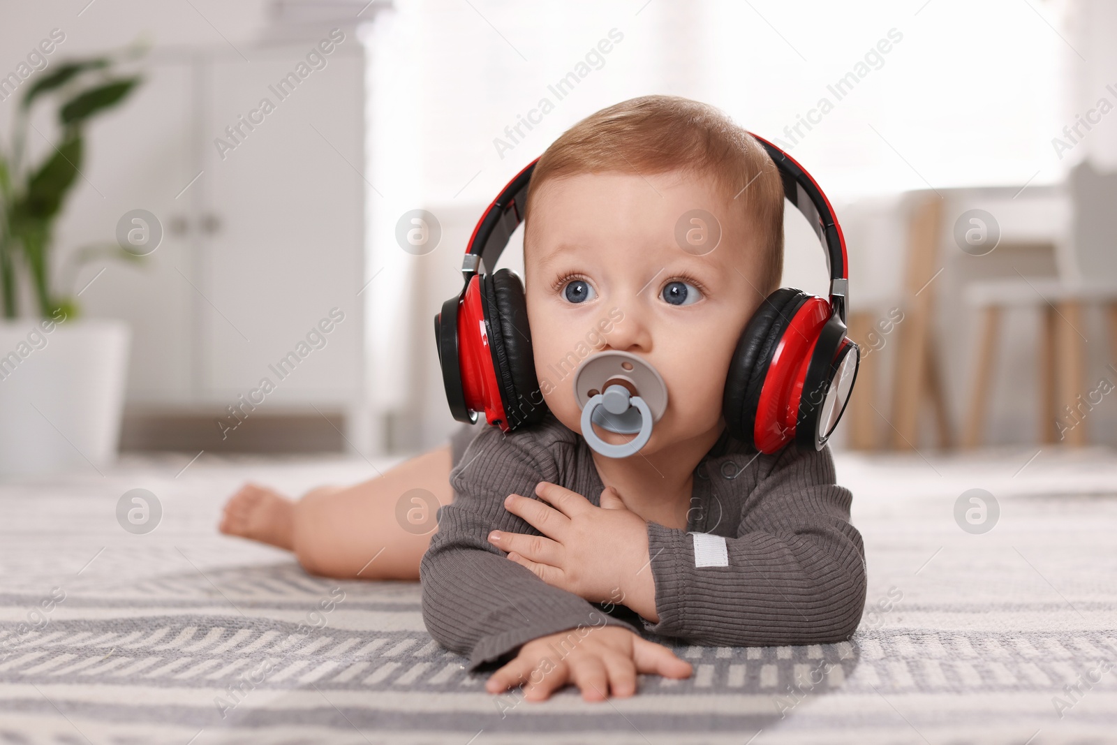 Photo of Cute little baby with pacifier and headphones on floor at home