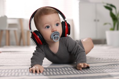 Cute little baby with pacifier and headphones on floor at home