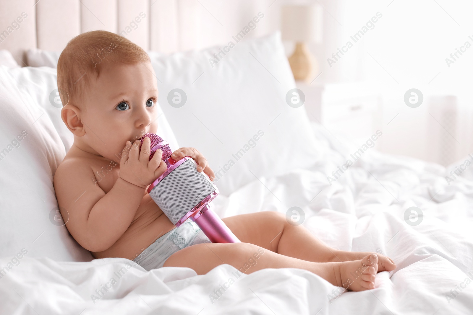 Photo of Cute little baby with microphone on bed at home, space for text