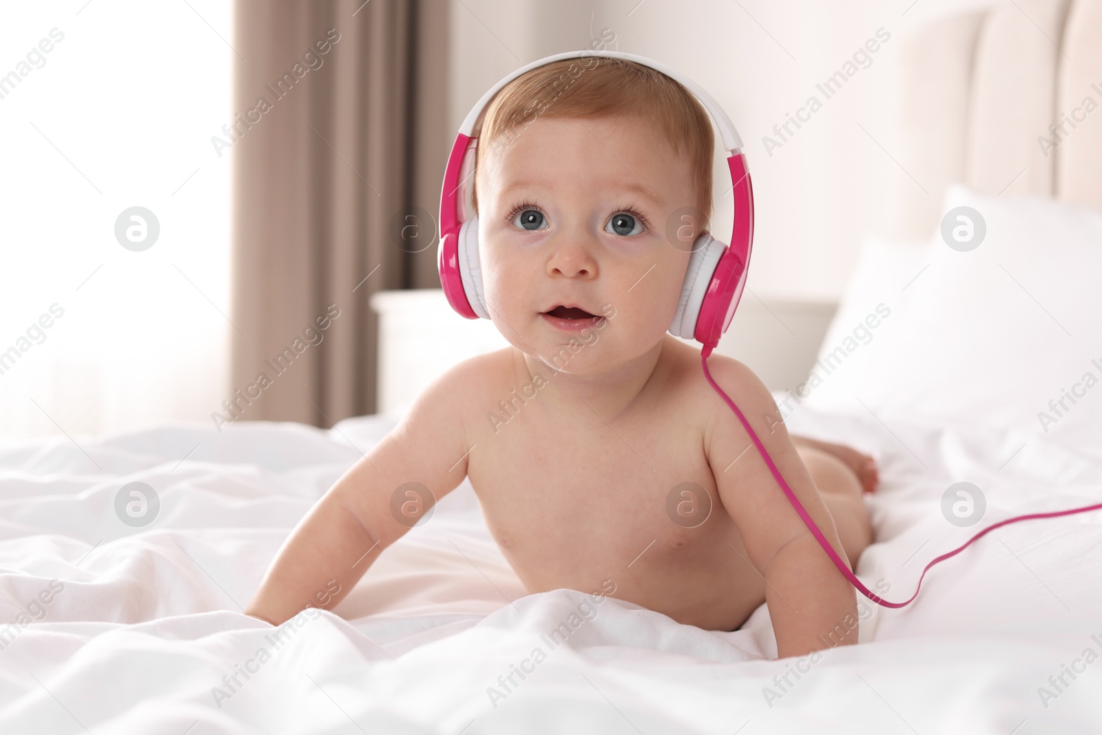 Photo of Cute little baby with headphones on bed at home