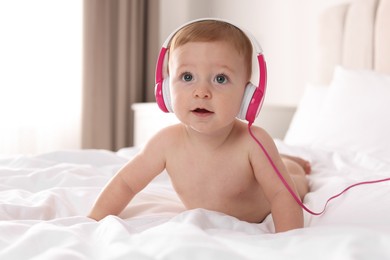 Photo of Cute little baby with headphones on bed at home