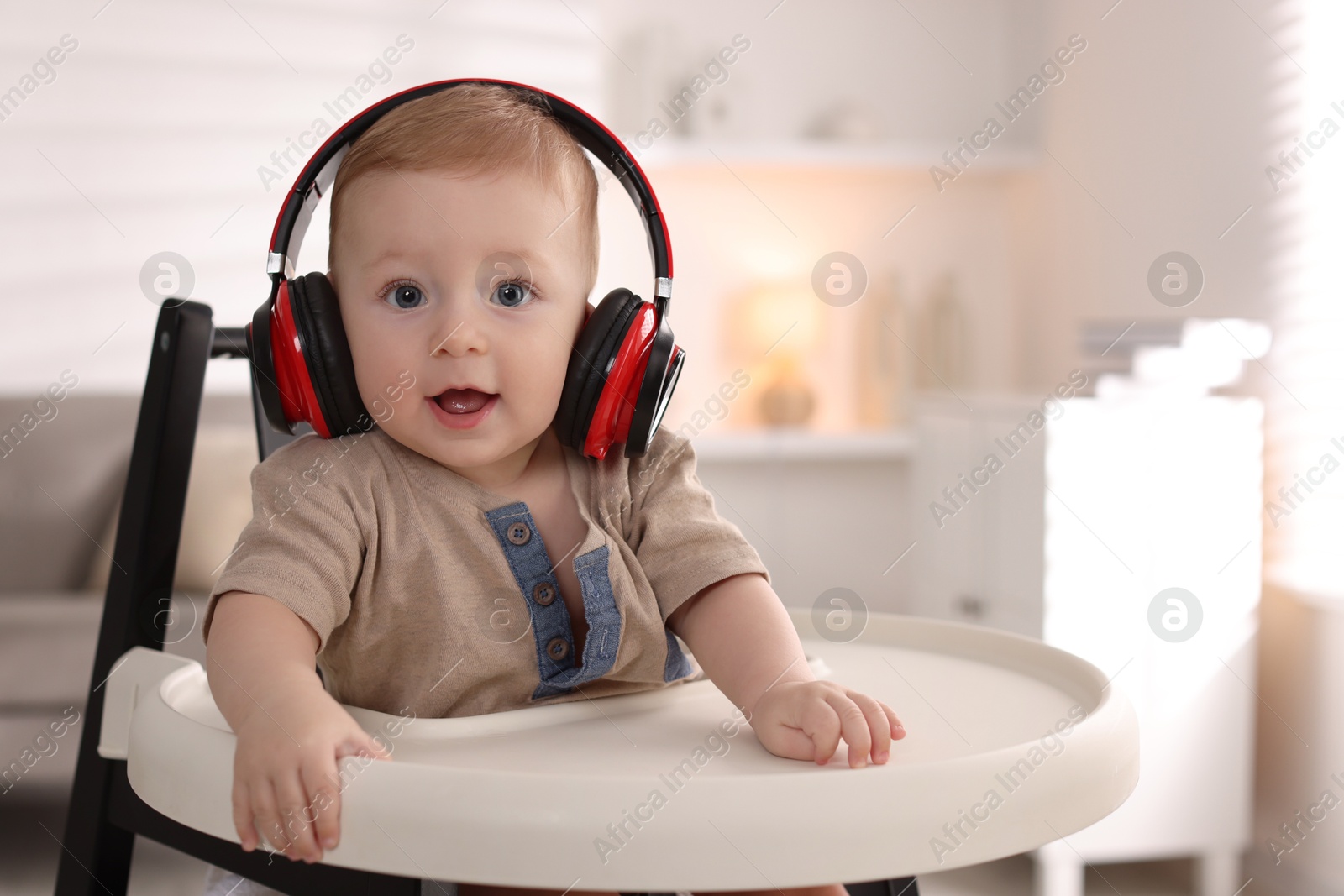 Photo of Cute little baby with headphones on high chair at home, space for text