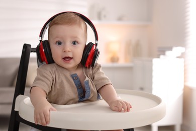 Cute little baby with headphones on high chair at home, space for text