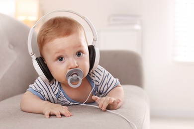 Photo of Cute little baby with headphones and pacifier on sofa at home, space for text