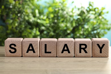 Photo of Word Salary made of cubes on light wooden table against blurred background, closeup. Space for text