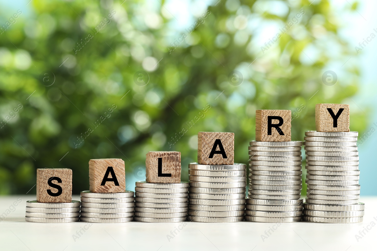 Photo of Word Salary made of cubes and stacked coins on white table against blurred background, closeup