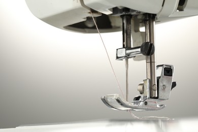 Photo of Sewing machine with white thread on light grey background, macro view. Space for text