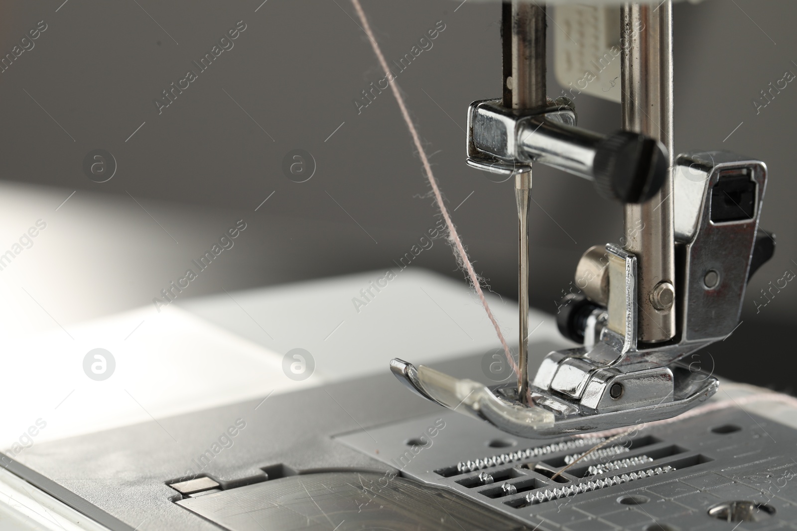 Photo of Sewing machine with white thread on light grey background, macro view. Space for text