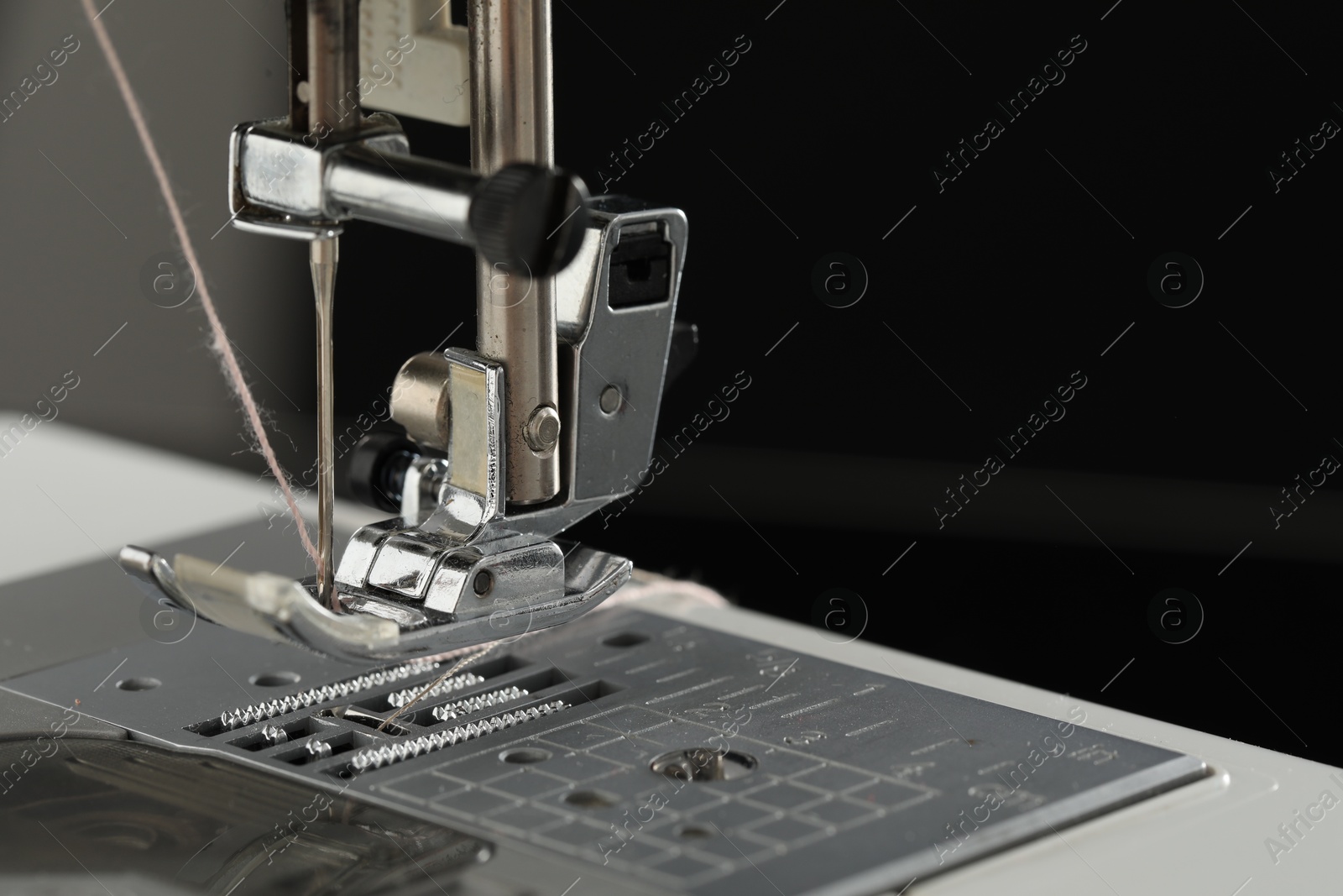 Photo of Sewing machine with thread on dark background, macro view. Space for text