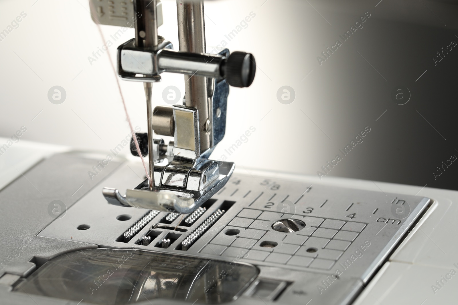 Photo of Sewing machine with white thread on light grey background, macro view. Space for text