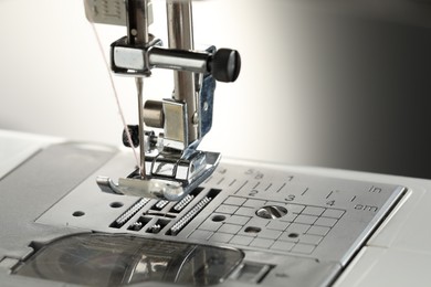 Photo of Sewing machine with white thread on light grey background, macro view. Space for text