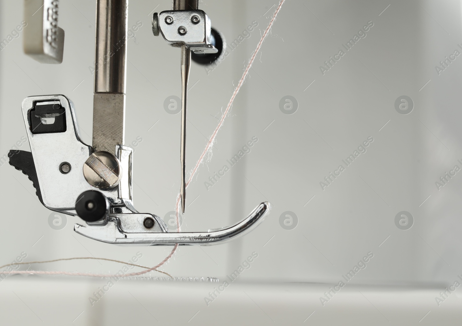 Photo of Sewing machine with white thread on light grey background, macro view. Space for text