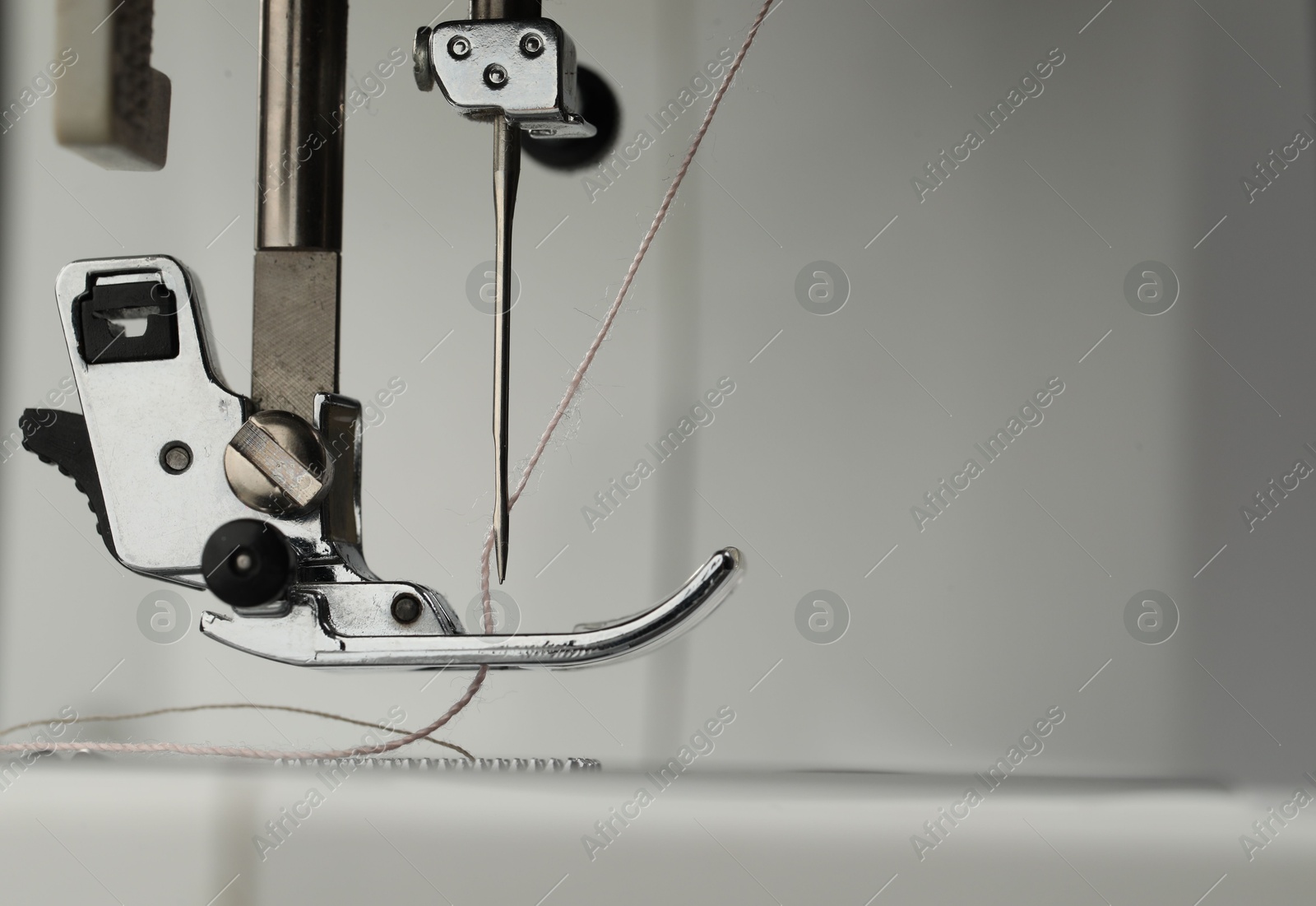 Photo of Sewing machine with white thread on light grey background, macro view. Space for text