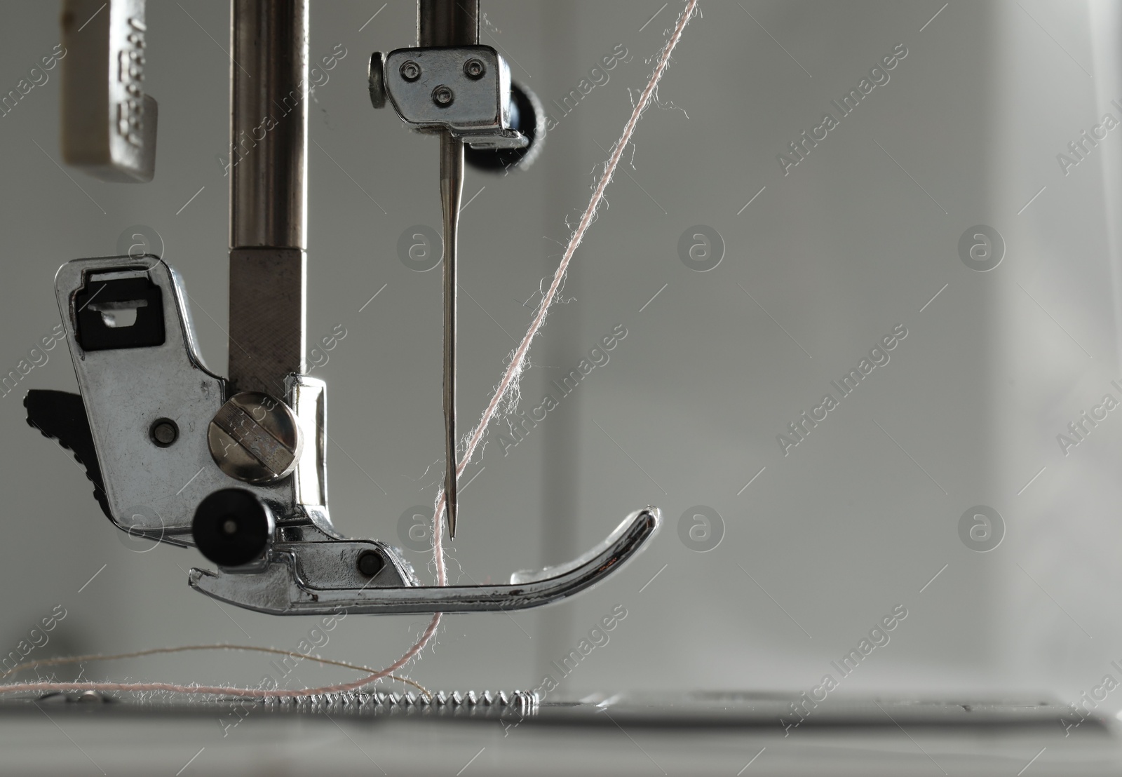 Photo of Sewing machine with white thread on light grey background, macro view. Space for text