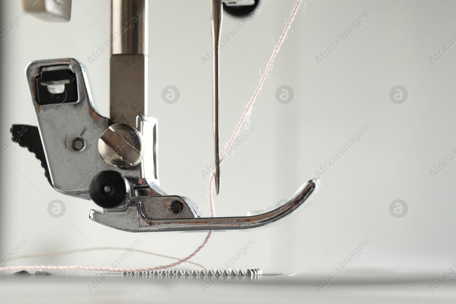 Photo of Sewing machine with white thread on light background, macro view