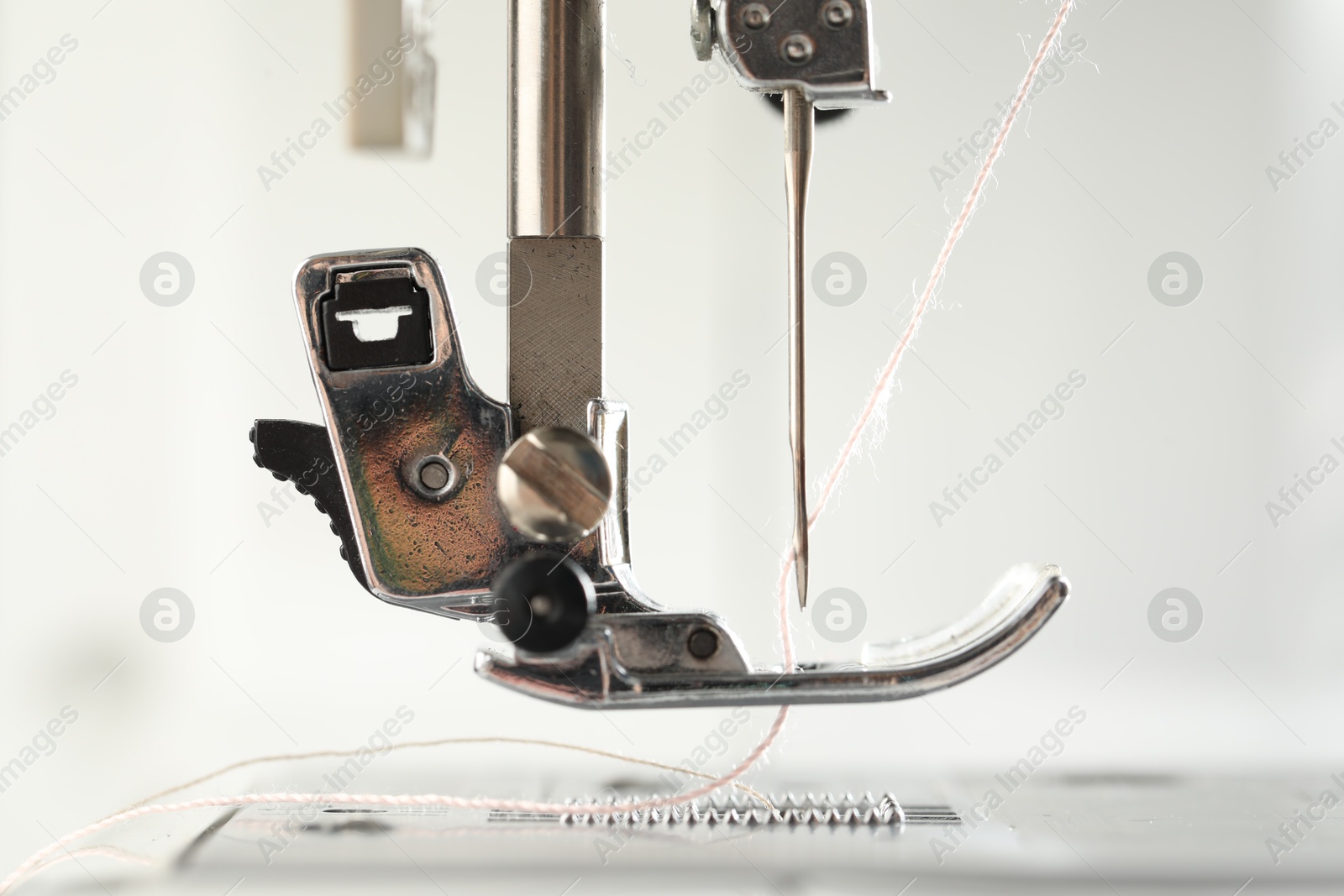 Photo of Sewing machine with white thread on light background, macro view