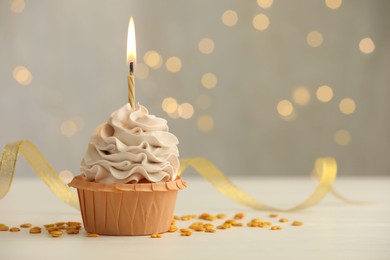 Photo of Birthday cupcake with burning candle on light table against blurred lights. Space for text