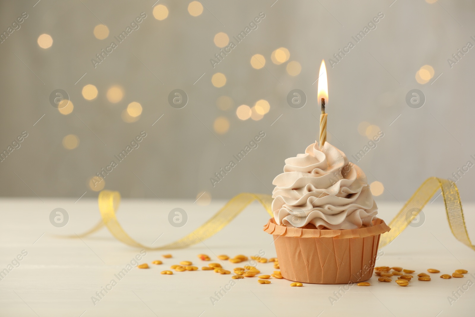 Photo of Birthday cupcake with burning candle on light table against blurred lights. Space for text