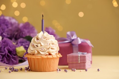 Photo of Birthday cupcake with candle, gifts and flowers on beige table against blurred lights, selective focus